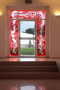 The sixth window, also surrounding exit doors, shows a tree and its thorny branches naked from leaves and fruits. It wraps the doorway in tangles.