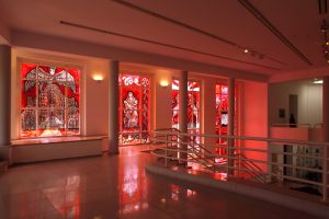 The gallery viewed from the upper level, red light flooding through the windows and into the space.