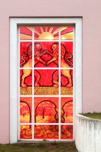 The window shows two lions standing against each other on a wall or aqueduct. They are painted in mirror image, as if they are in battle. The lions reference the Aryeh Yehuda (the Lion of Judah) of the municipal emblem of the city of Jerusalem. At the bottom of the painting, the snake has begun to climb and wrap one of the pillars holding the aqueduct arches. Above the lions’ fight scene appears a sun with rays shooting outward; it is unclear whether it is setting or shining. Through the arches of the aqueduct, in the background, there is a barren wasteland covered with a few burnt trees.