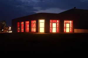 The exterior of the gallery viewed at night. The gallery glows red, thanks to the artificial light inside the gallery and the darkness that covers it from the outside.