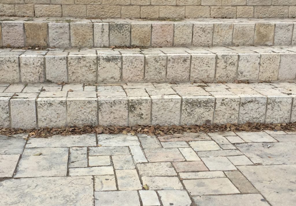 Photograph of a floor, three steps, and wall of Jerusalem stone.
